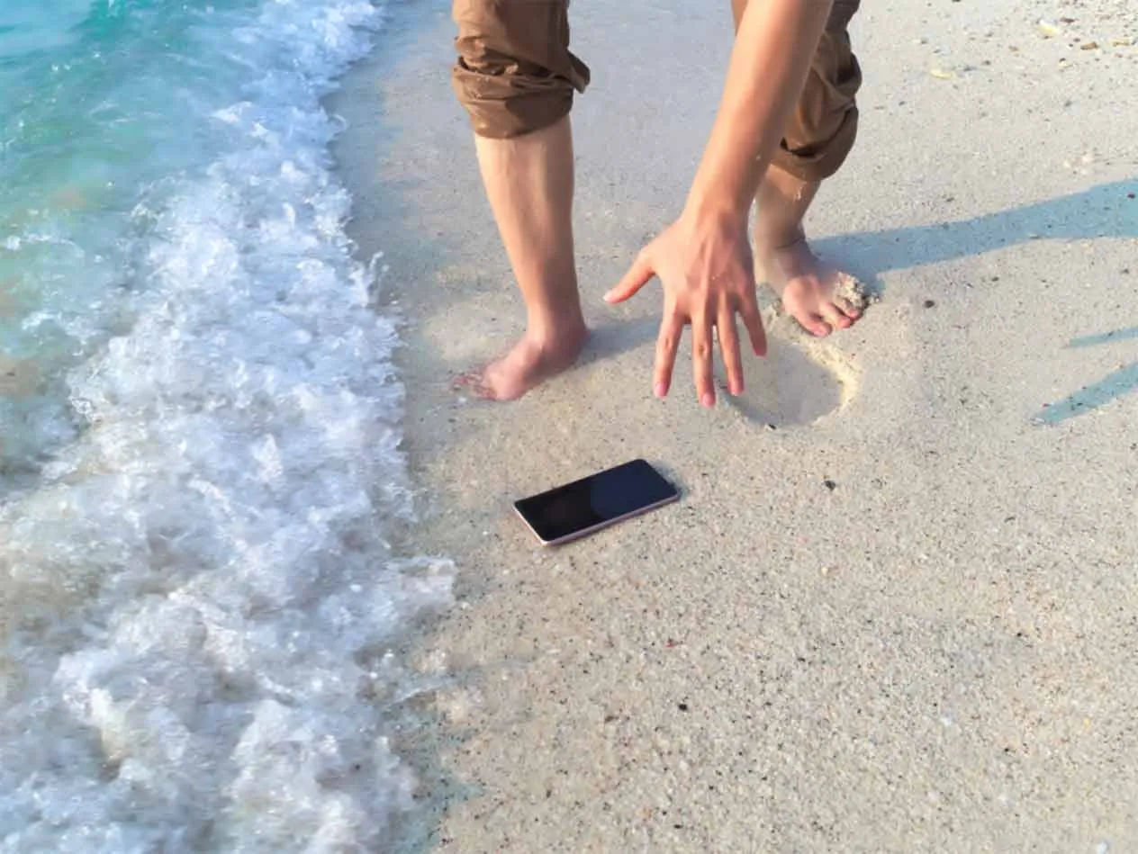 Mężczyzna schylający się po telefon leżący na plaży